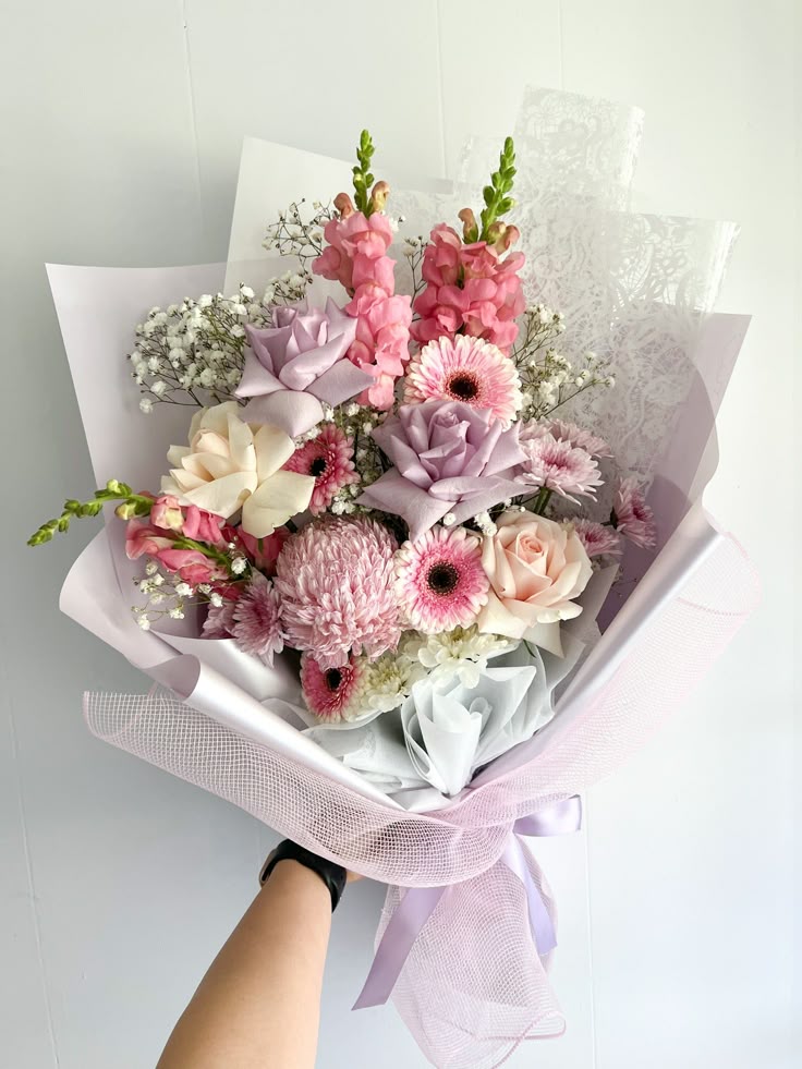 A soft pink Mother's Day bouquet with gerbera daisies, roses, and baby's breath wrapped in white paper