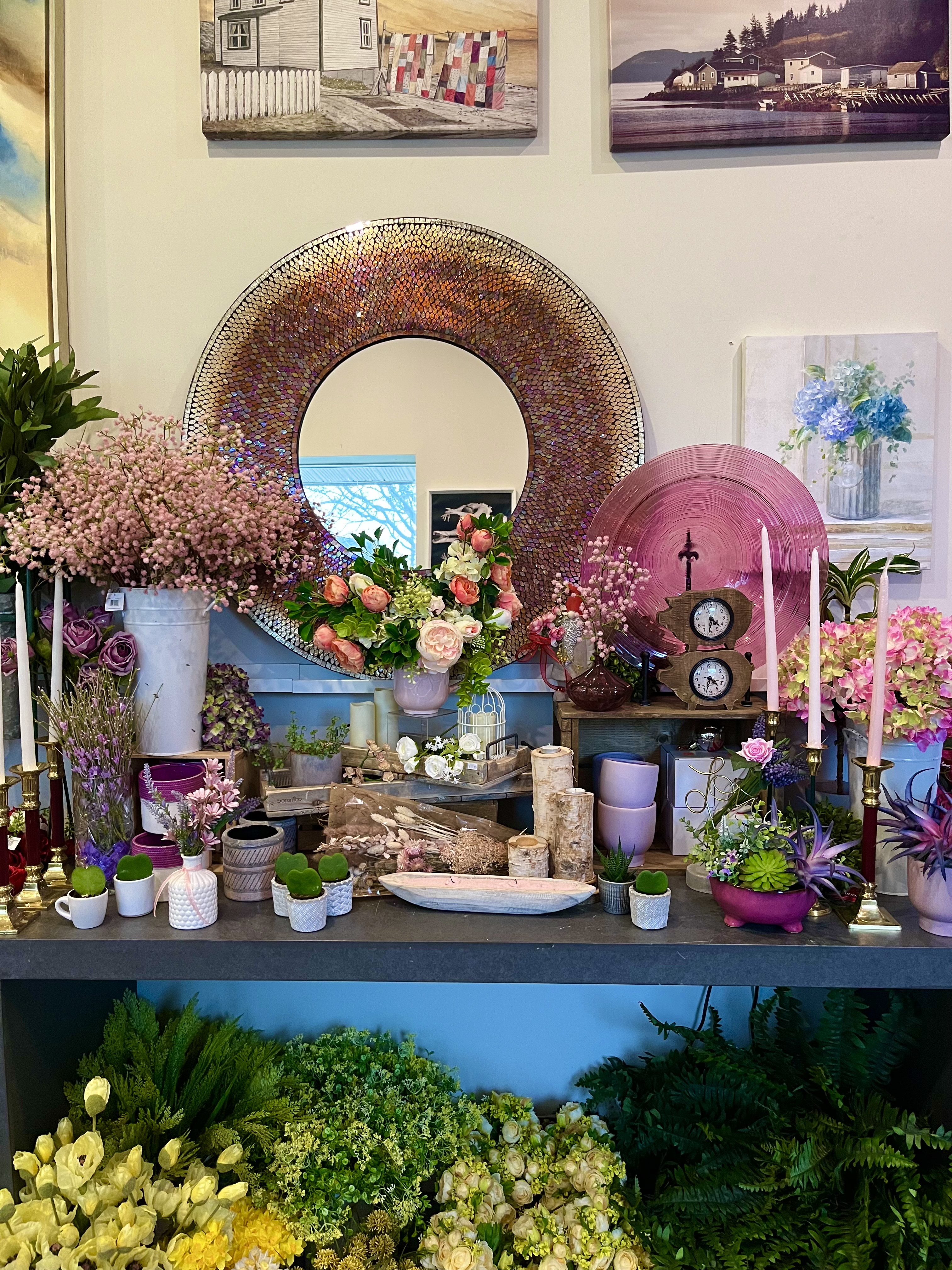 A pink-toned corner of the shop featuring a round mirror, roses, candles, and small potted plants